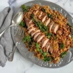 A platter of pork tenderloin and sauerkraut is garnished with sautéed kale and black-eyed peas. Arranged on a platter.