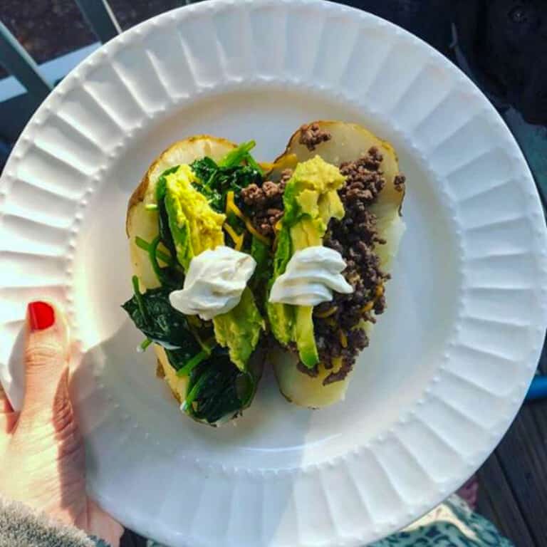 Baked potato halves with avocado and sour cream on a white plate.