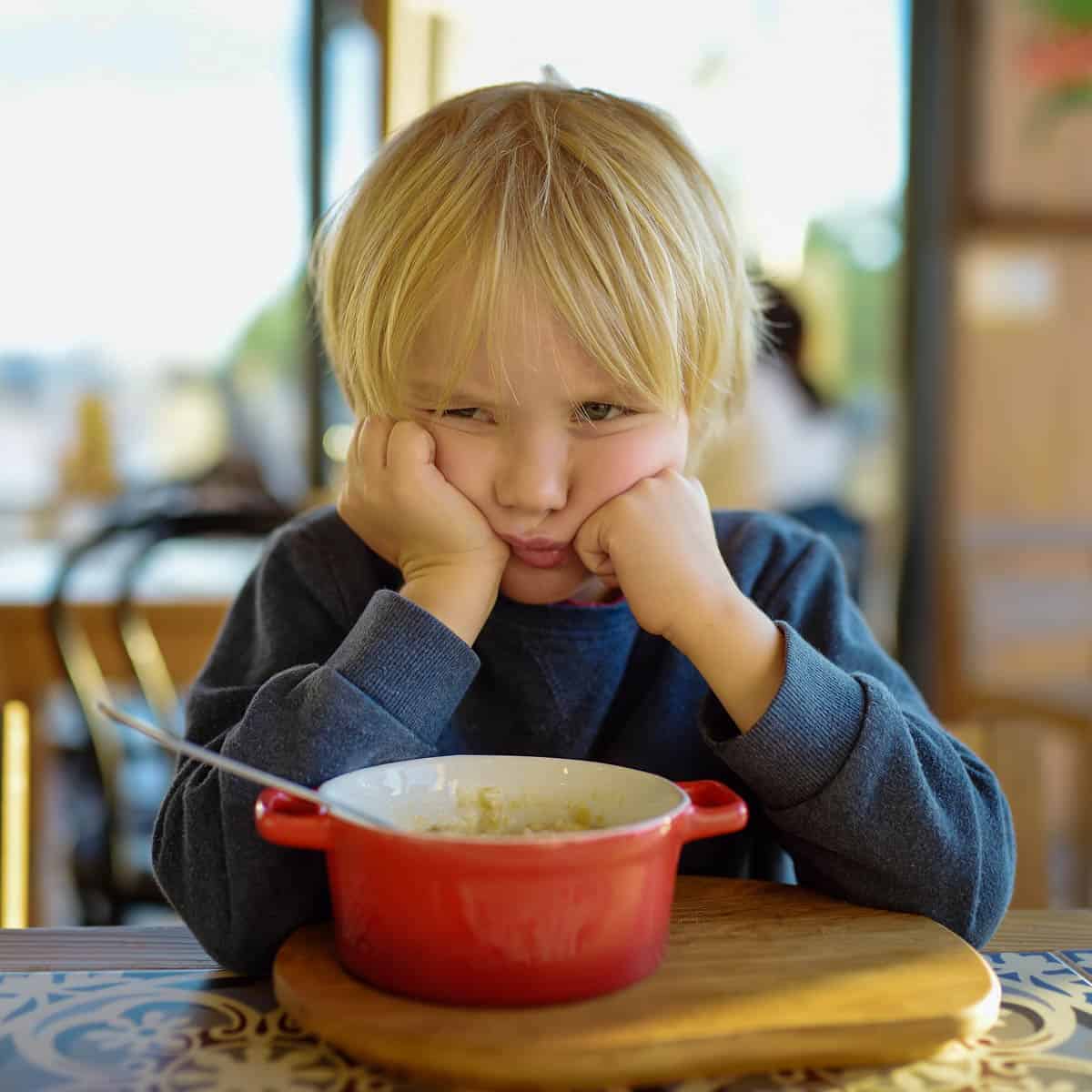 Little child sitting the table in cafe or restaurant and doesn't want to eat.