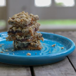 4 chocolate, caramel oat bars on a bright blue plate.