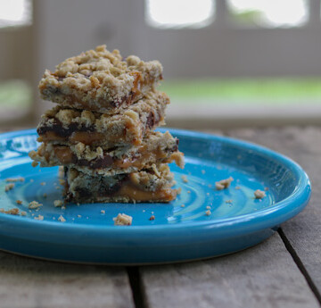 4 chocolate, caramel oat bars on a bright blue plate.