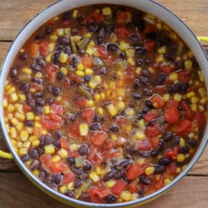 Large, yellow pot filled with black beans, tomatoes and corn.