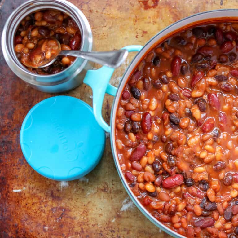 Baked beans in a thermos with a blue lid and in a light blue pot with a rustic metal background.