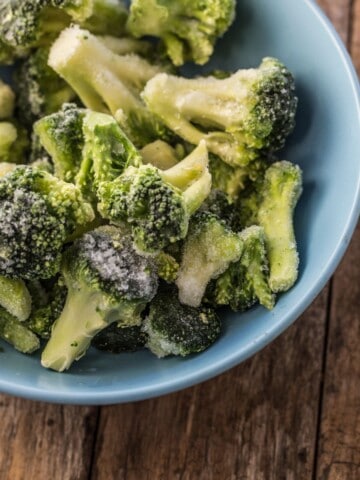 Frozen broccoli florets in a cornflower blue bowl on a rustic wooden surface.