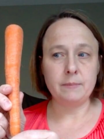 Woman in a red shirt holds up carrot.