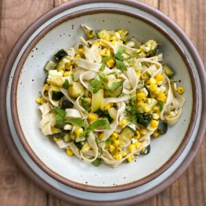 Pasta with zucchini, corn, and cilantro served in an East Fork everyday bowl on an East Fork dinner plate, both in eggshell.
