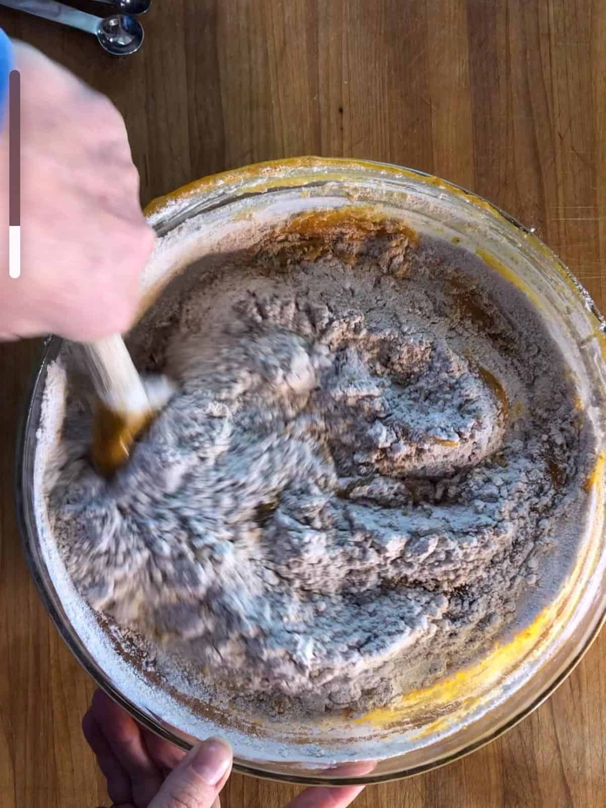 A glass bowl in which the flour and spice mixture is being added to the wet ingredients of the pumpkin spice bread batter.