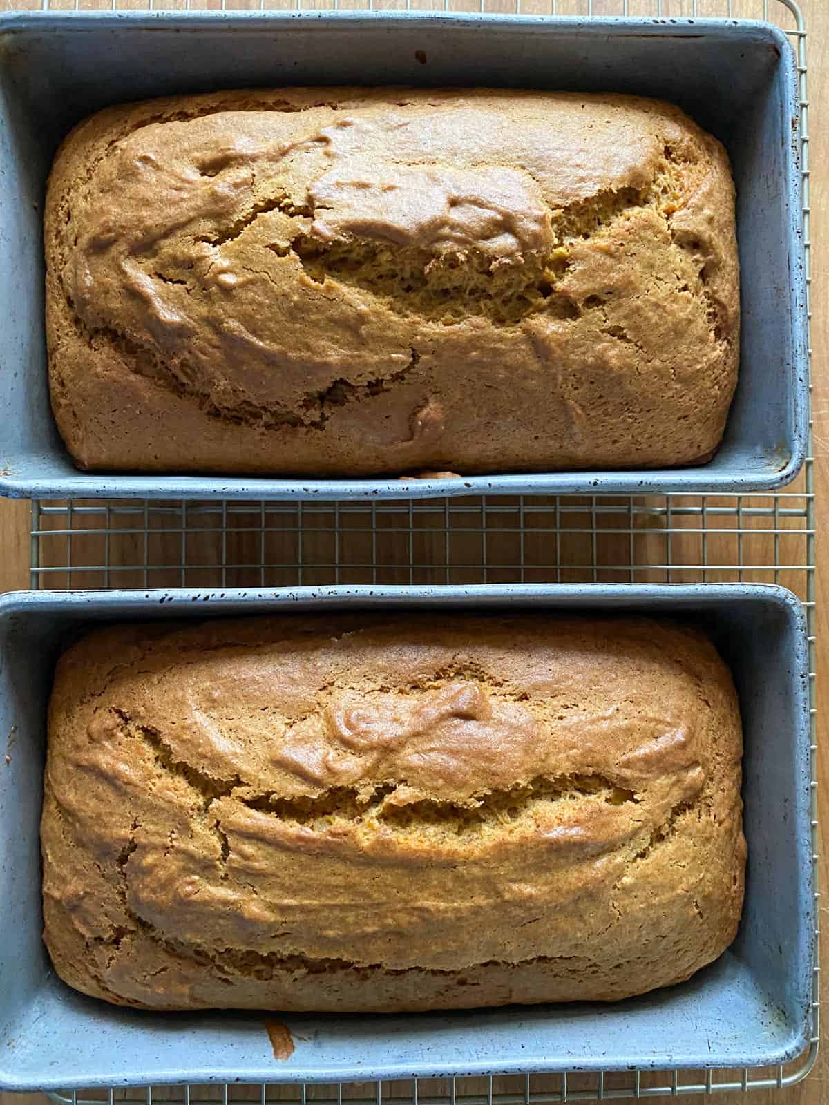 Two loaves of spiced pumpkin bread in metal baking pans resting on a cooling rack. 