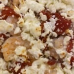 A close up picture of cooked shrimp, feta, and roasted red peppers.