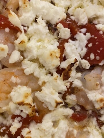A close up picture of cooked shrimp, feta, and roasted red peppers.