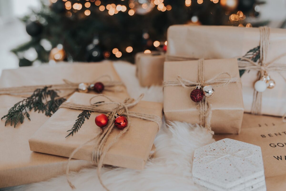 Christmas gifts wrapped in brown paper, tied with twine and decorated with greenery and small Christmas ornaments. 