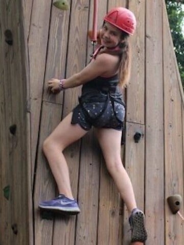 Girl climbing on a rock wall, looking over her shoulder to smile for the camera.