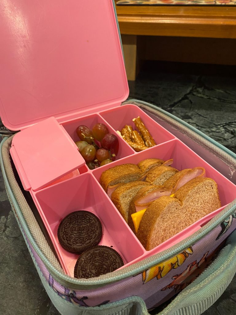Bento-Lunchbox von Pottery Barn mit einem Sandwich, Oreo-Keksen, Brezeln und Weintrauben. 