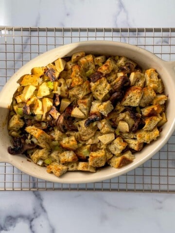Rosemary Sourdough Mushroom Stuffing in an oval dish sitting atop a cooling rack on a marble countertop.