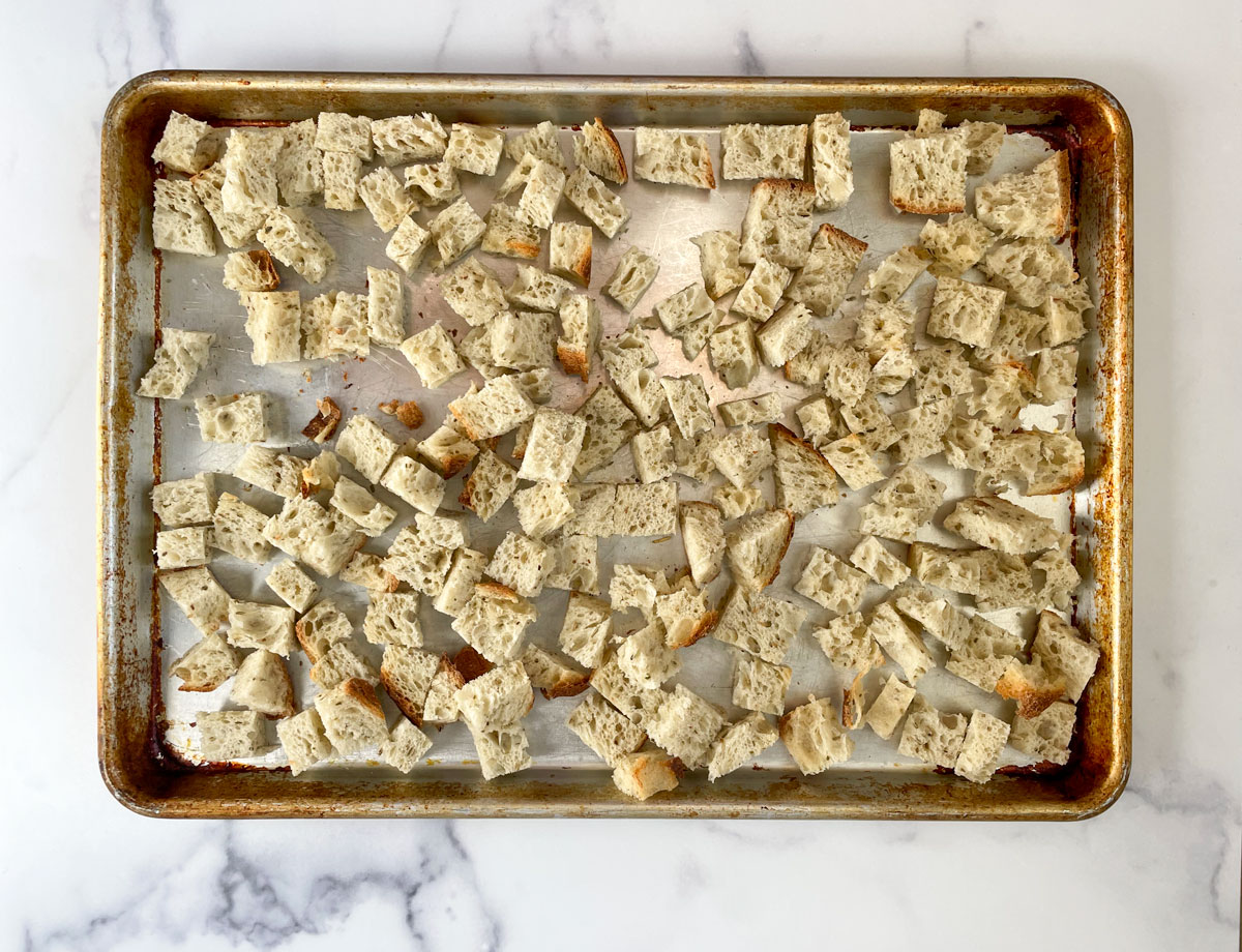 Tosted bread cubes on a sheet pan on a marble counter