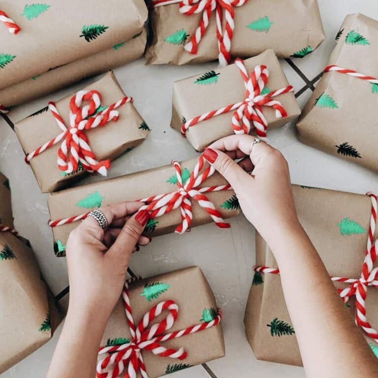 2 hands tying a red and white blow on a gift in brown paper.