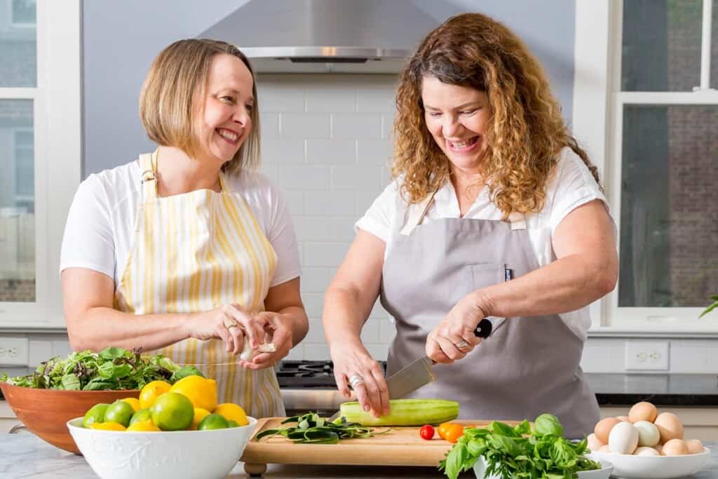 Two females standing at a kitchen counter making a salad.