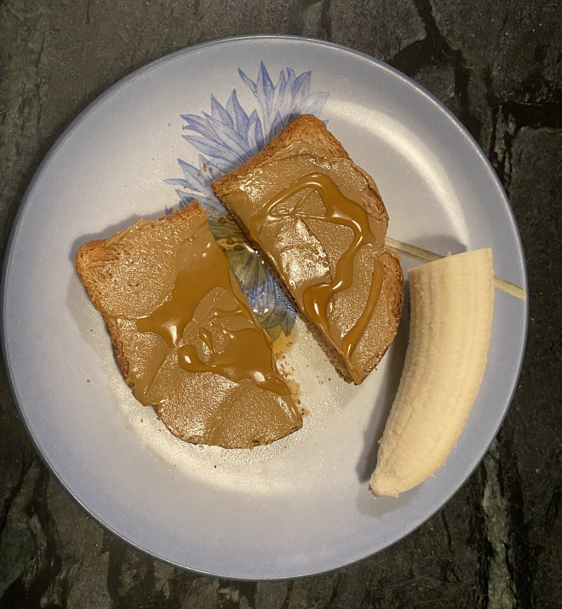 Blue plate with a piece of toast topped with sunflower seed butter and honey, and a half of a banana on the side.