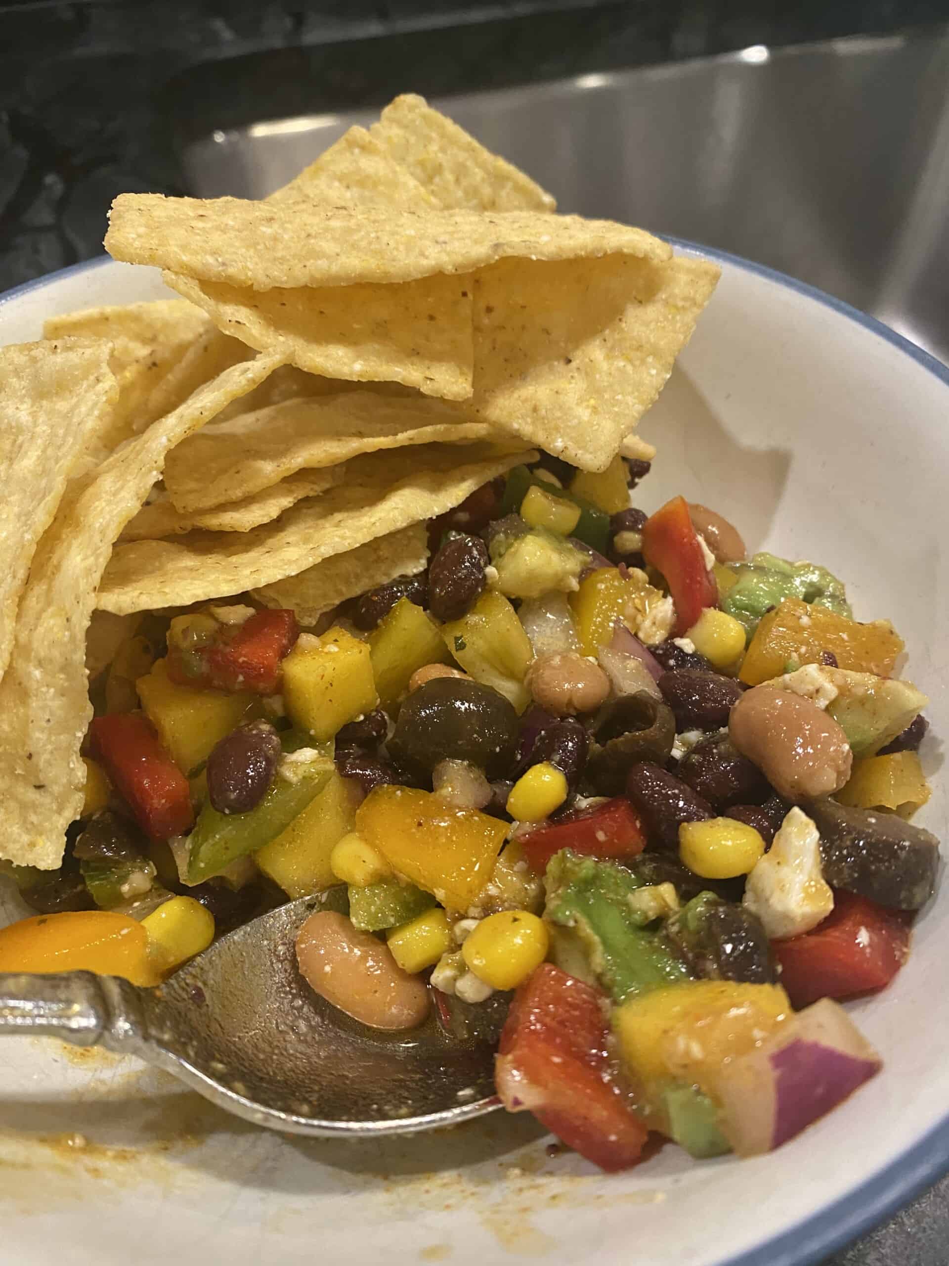 White bowl with blue rim filled with a bean salsa and tortilla chips