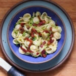 Orechiette pasta with bacon and Brussels sprouts in a lapis blue bowl on a light blue plate.