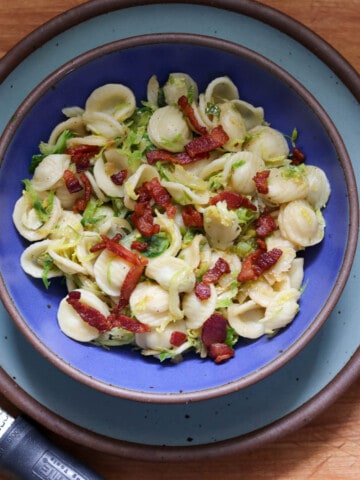 Orechiette pasta with bacon and Brussels sprouts in a lapis blue bowl on a light blue plate.