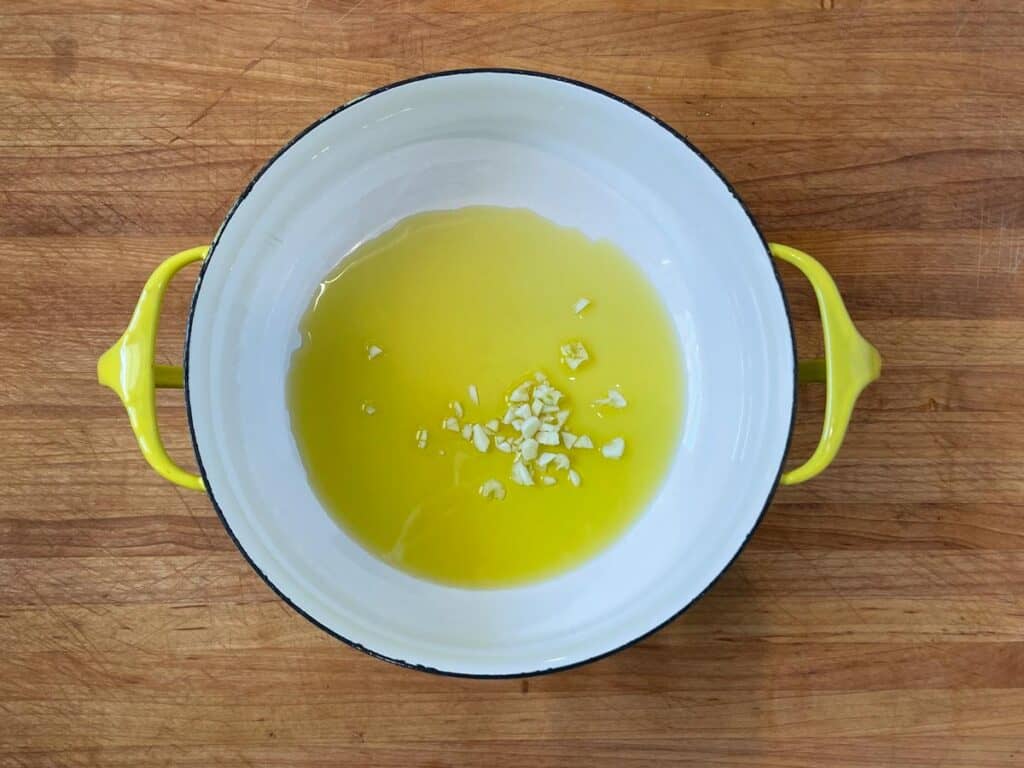 Olive oil and chopped garlic in a yellow Danske enamel pot.