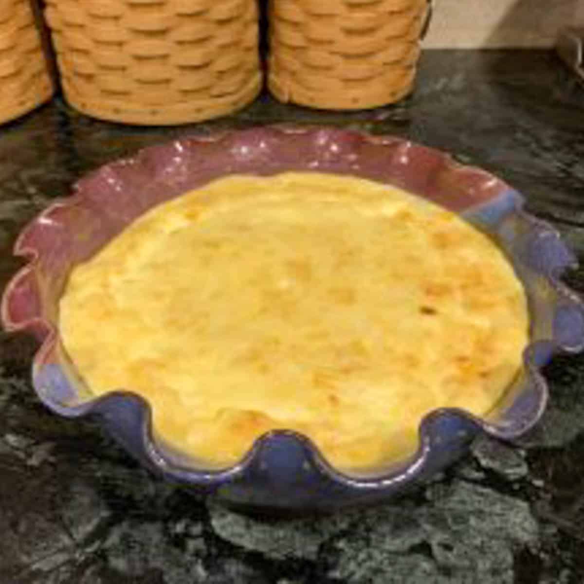 Baked corn pudding in a round pottery dish with fluted edges.