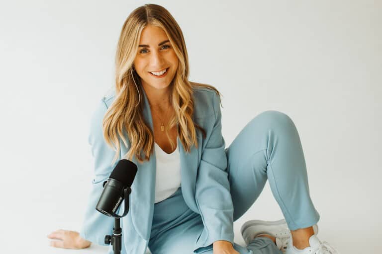 Woman with long blond hair in a light blue suit site on the floor in front of a microphone.