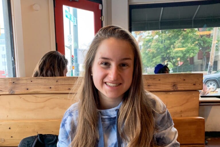 Young woman with long blond hair sits at a table with several bowls of food. She smiles for the camera.