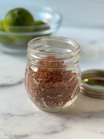 Homemade Mild Taco Seasoning in a glass jar on a marble countertop.