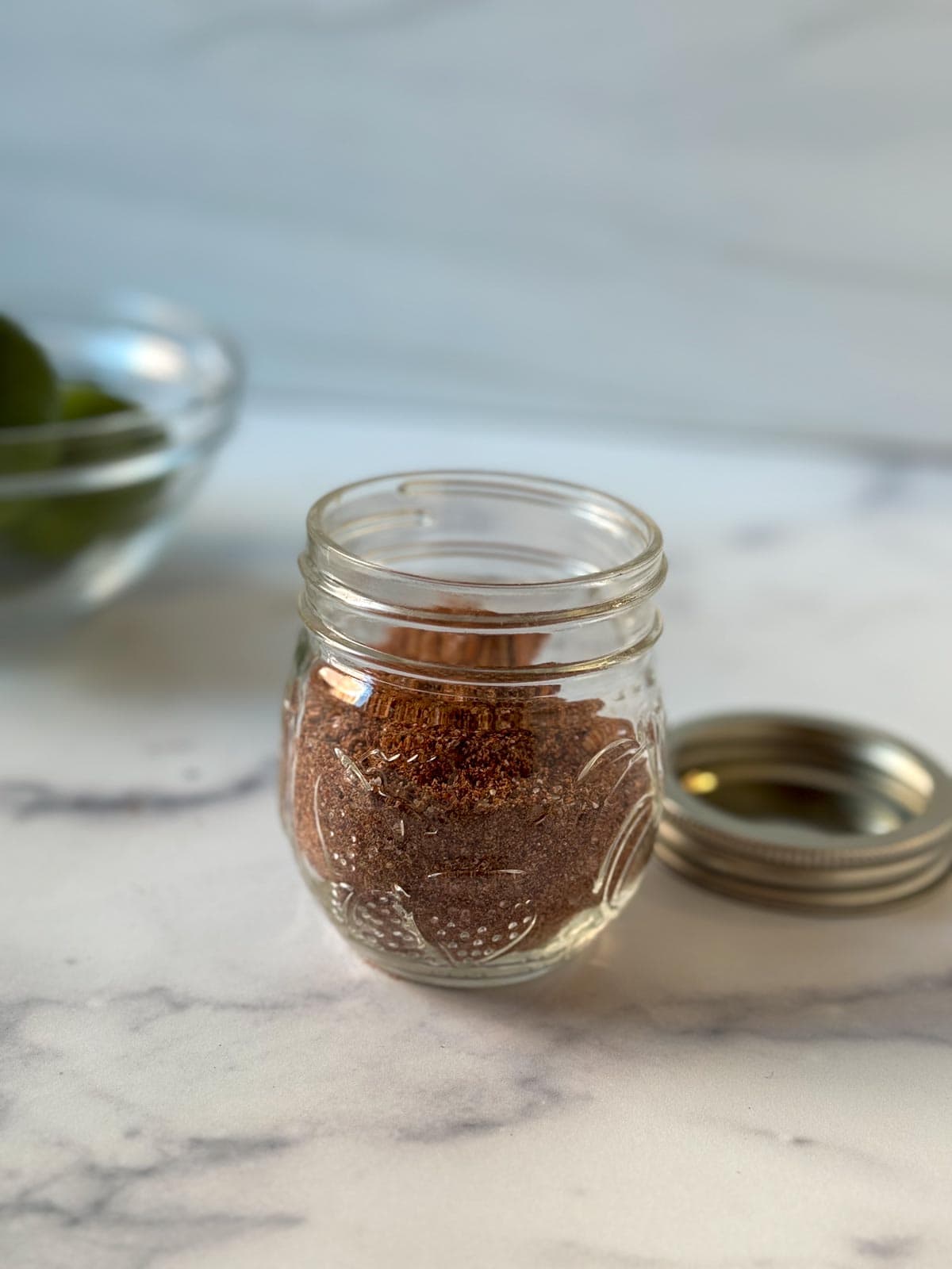 A glass jar filled with homemade taco seasoning on a countertop.