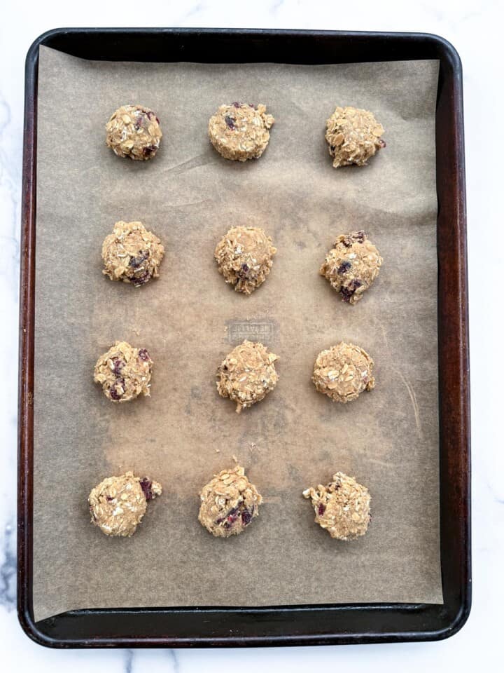 Slightly flattened oatmeal craisin cookie dough balls on a parchment lined half sheet pan.