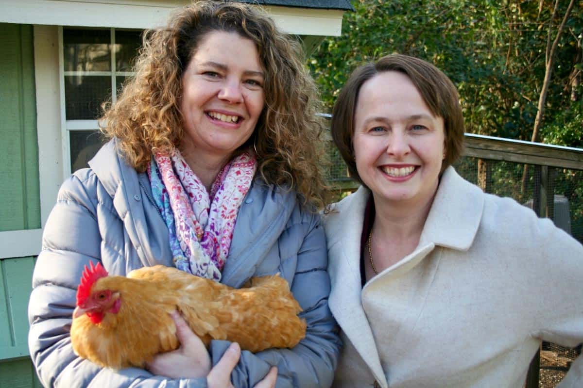 Two adult females outdoors on a cold day. One female is holding a chicken.
