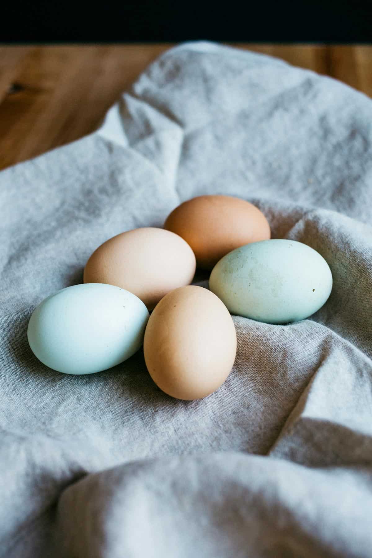 Different colored eggs on a gray linen towel.