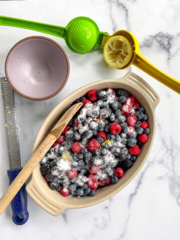 Mixed berries, sugar, and lemon zest for making mixed berry cobbler in a 9 x 11 inch oval dish. 