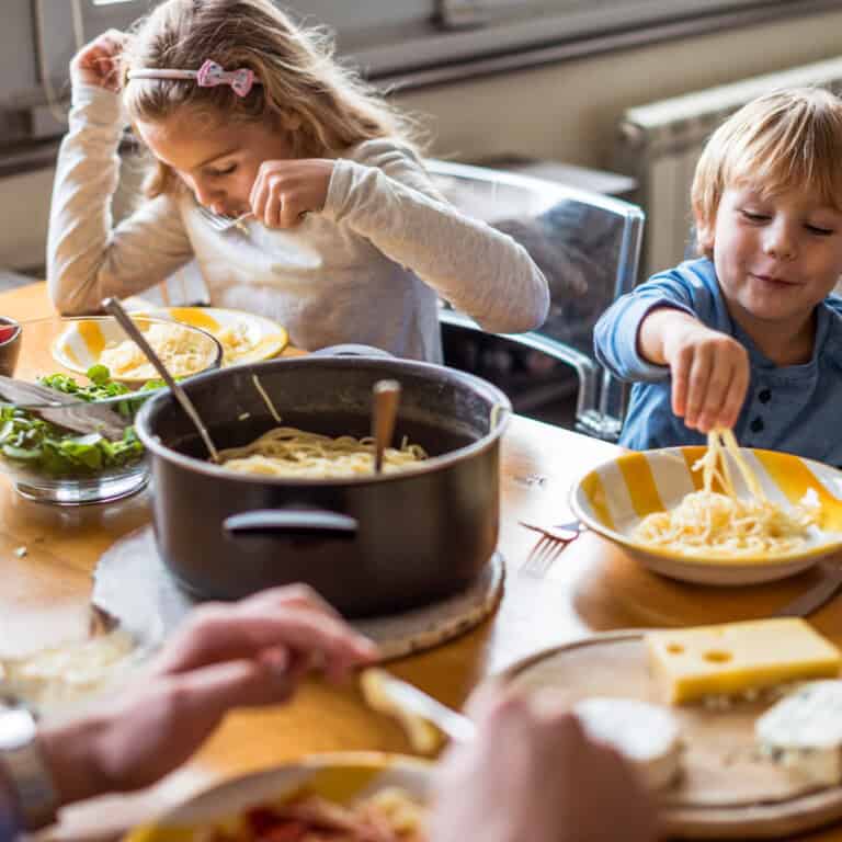 2 kids with blond hair eating a meal.