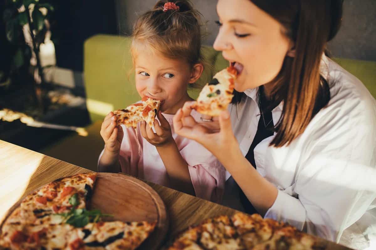 Young girl eating pizza with mom.