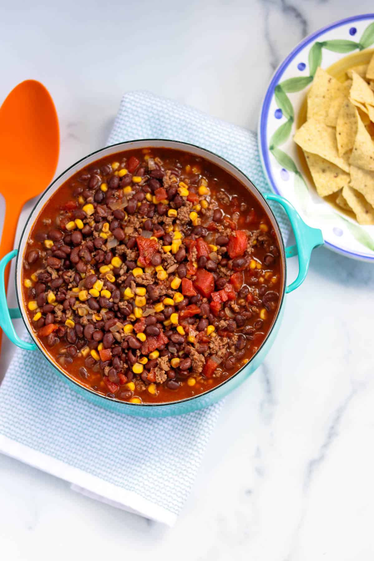 Fished pot of easy black bean taco soup in a light blue Dansk pot next to a bowl of tortilla chips and an orange serving spoon.