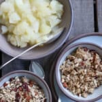 Three bowls on a wooden surface: one with cooked apples and the other two filled with granola.