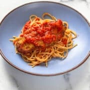 Blue plate with spaghetti topped with a breaded chicken parmesan and red tomato sauce, on a marble surface.