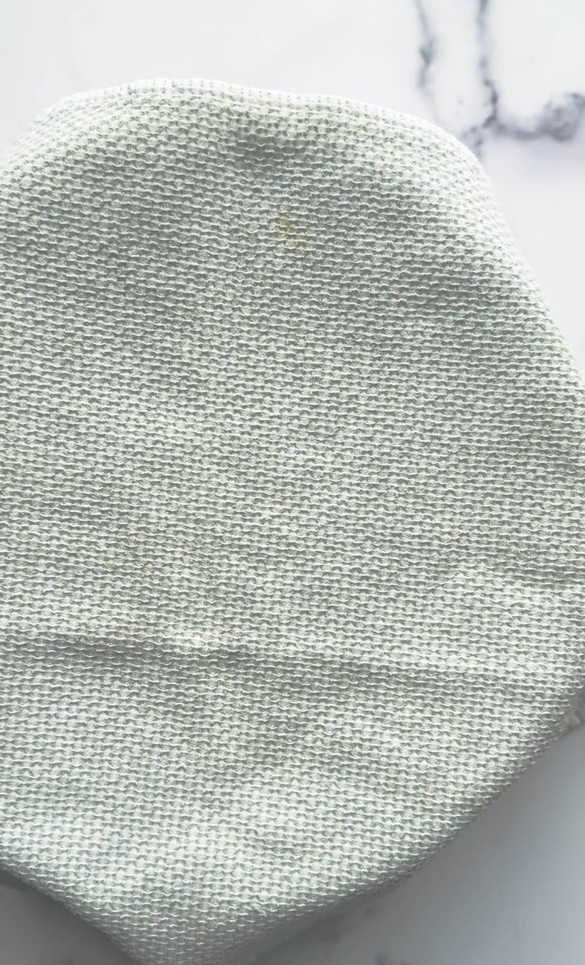 A round bowl covered with a textured, light gray fabric on a white marble surface.
