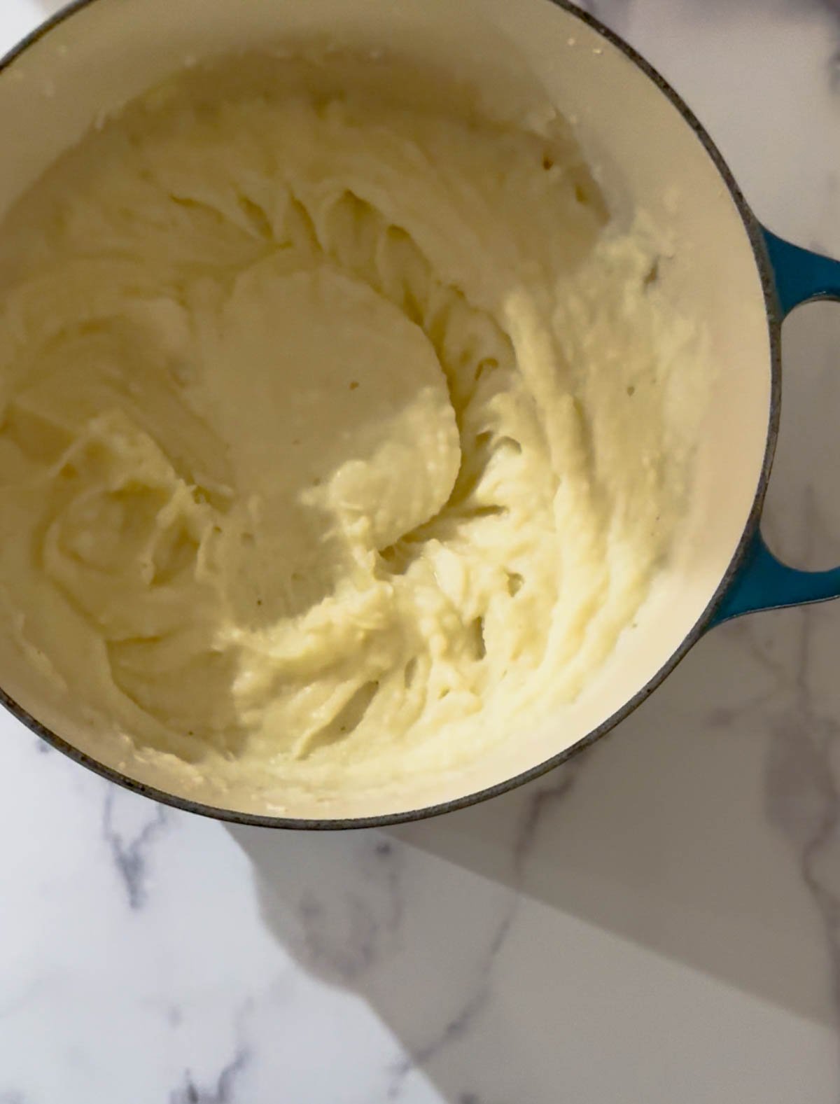A blue pot filled with creamy, whipped mashed potatoes sits on a white marble surface.