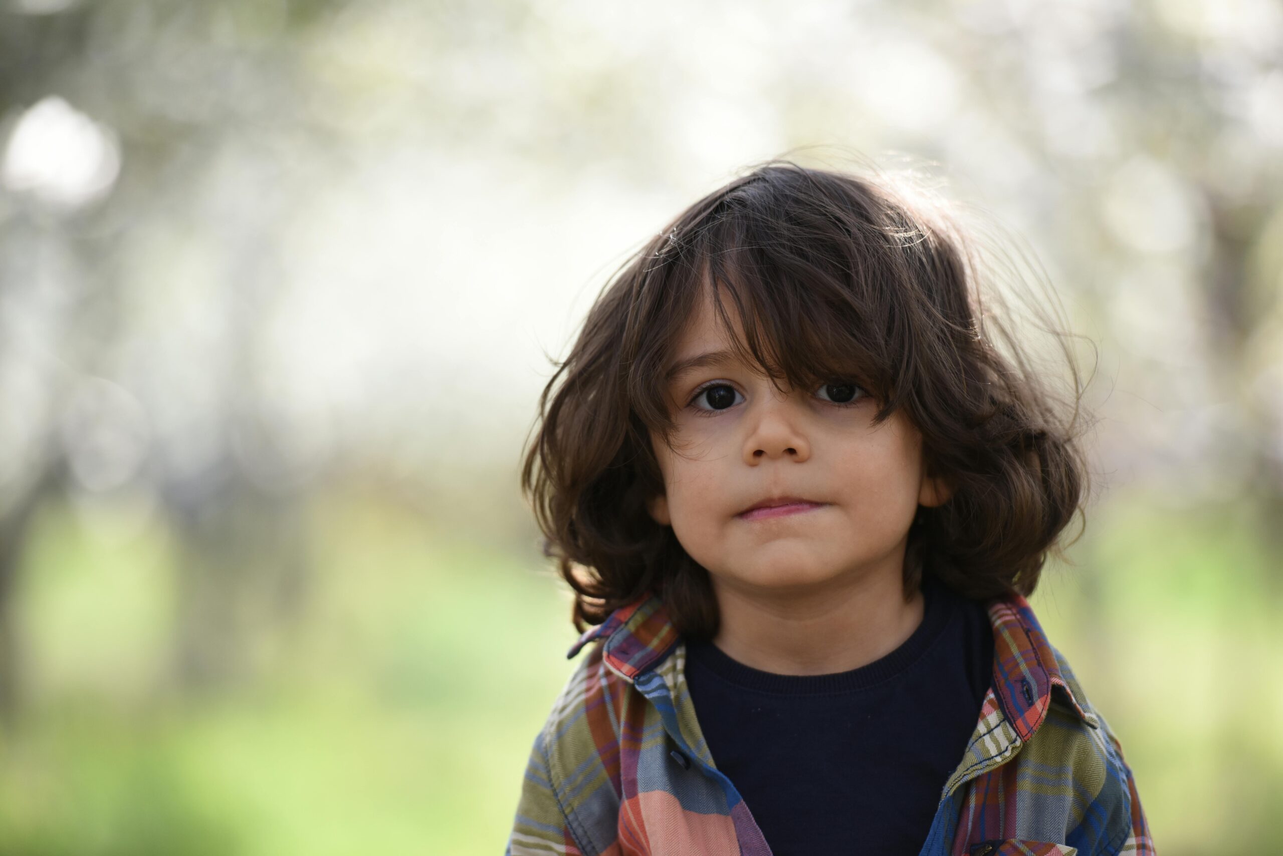 A young child with long brown hair and a plaid shirt stands outdoors, looking at the camera—perfect for interpreting growth charts amid blurred greenery and soft sunlight.